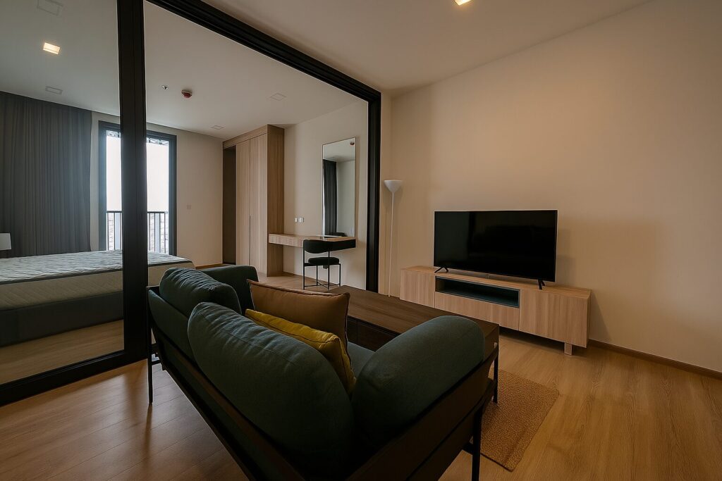 Modern one-bedroom condominium unit at XT Phayathai featuring open-plan living area with stylish sofa, smart TV, light wood flooring.